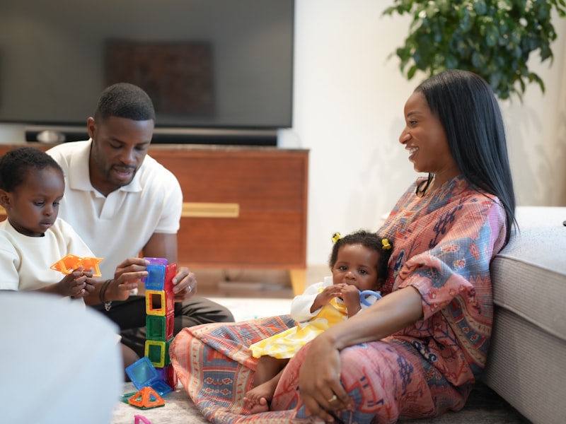 A mum and dad building blocks on the living room floor with their toddler and baby