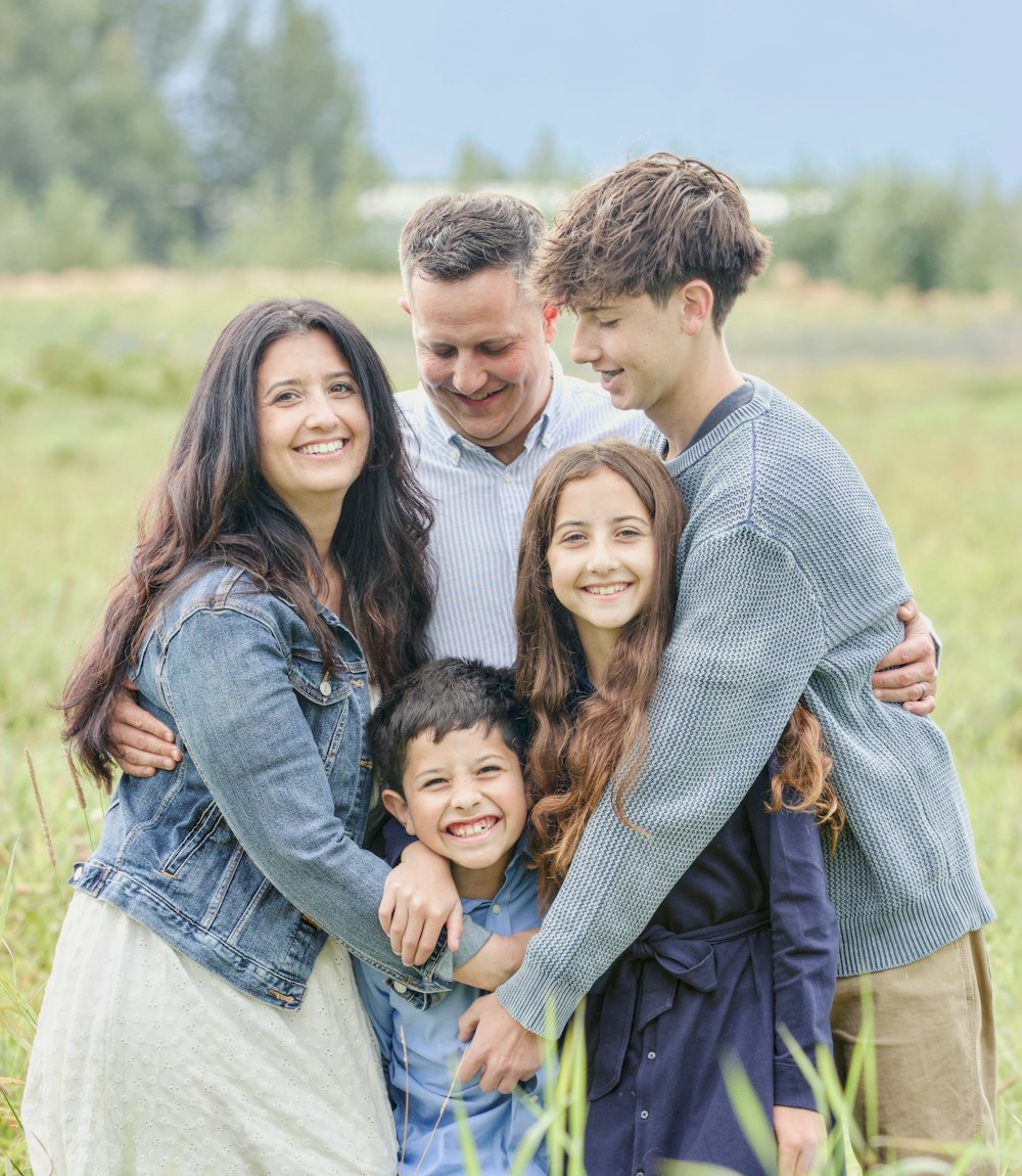 A mum, dad, teenage son, daughter and young boy hugging together in a summer field